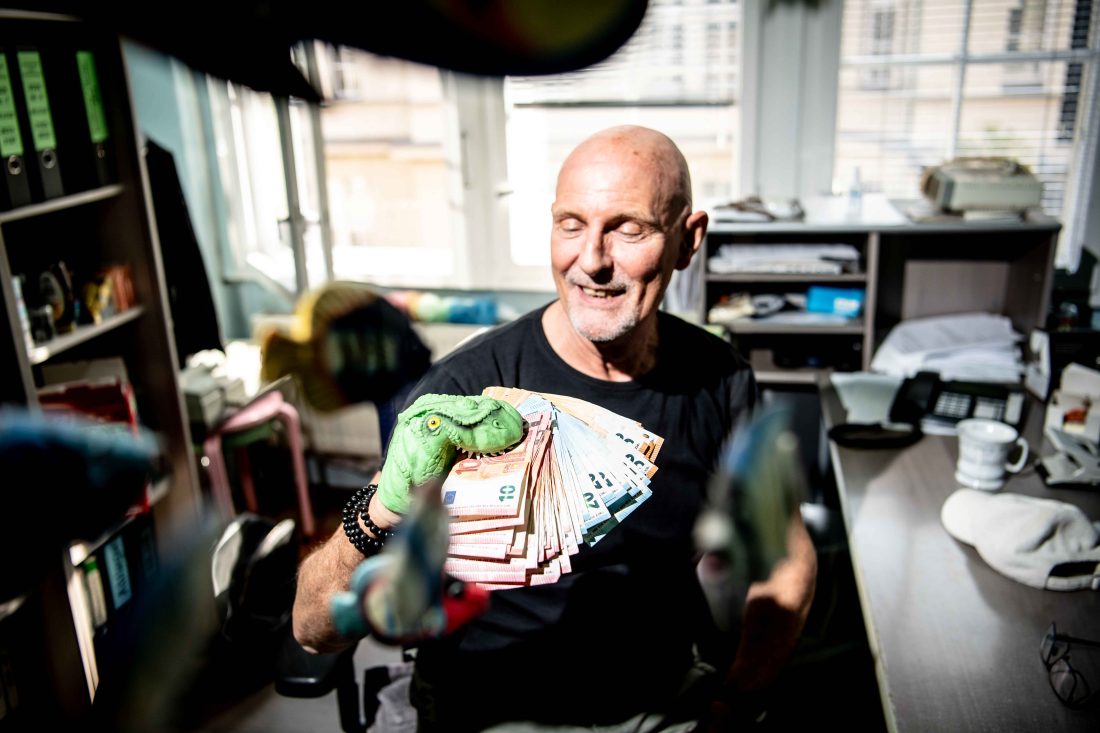 Porträt von Josef Mratschnigger, in seiner Hand eine Dino-Puppensocke, die einen Stapel Geldscheine frisst