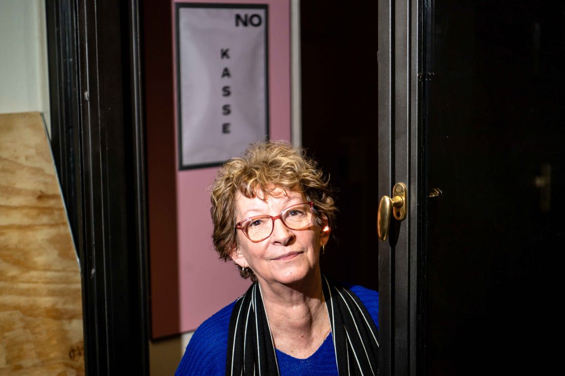 Porträt von Martine Klein, hinter ihr ein Schild mit der Aufschrift "KASSE"