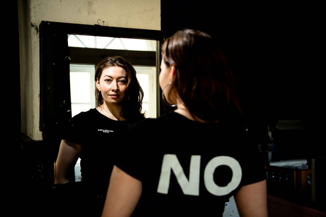 Porträt von Vanda Hehr, die ein NO-T-Shirt trägt und über einen Spiegel in die Kamera schaut